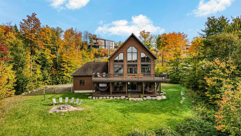 Vue aérienne d'un chalet en bois aux grandes fenêtres, entouré d'arbres aux couleurs d'automne
