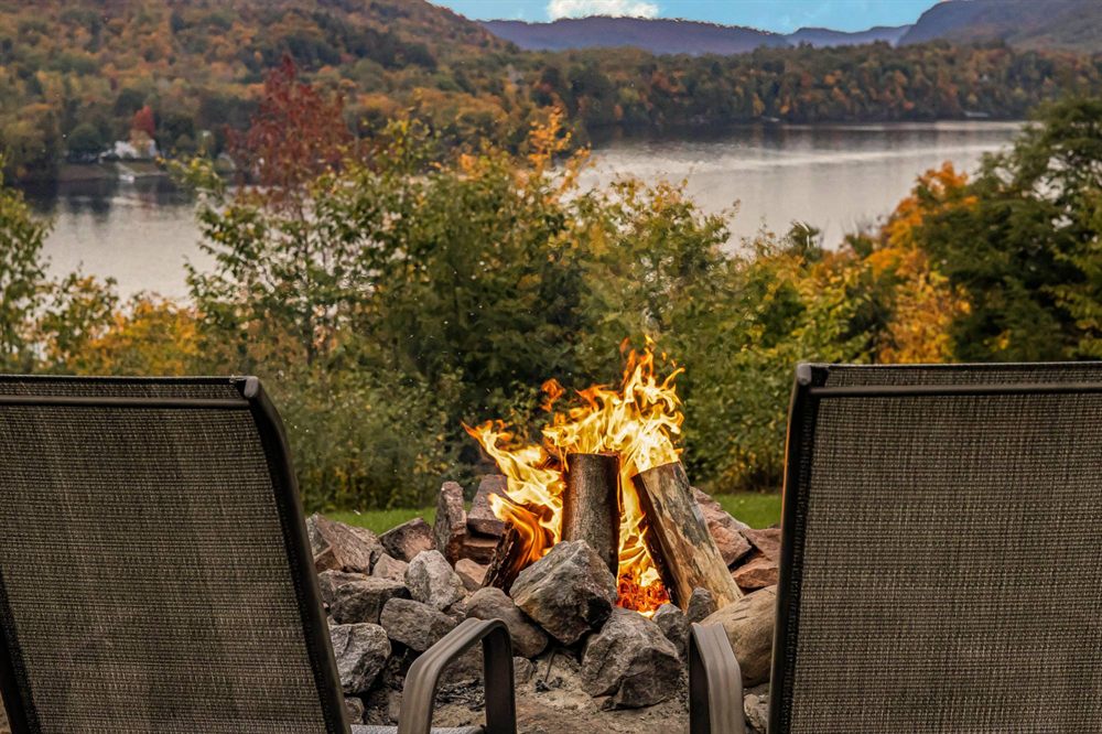 Deux chaises devant un feu de camp avec vue sur le lac en automne