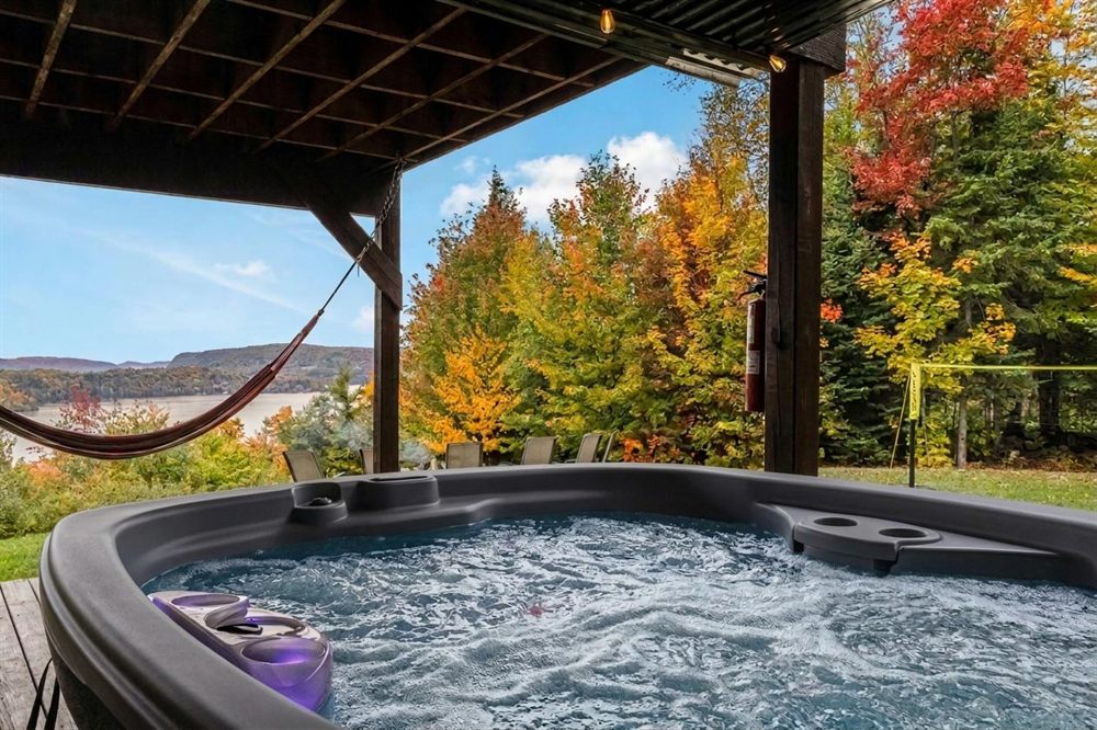 Spa extérieur sous la terrasse couverte avec vue sur le lac et la forêt en automne